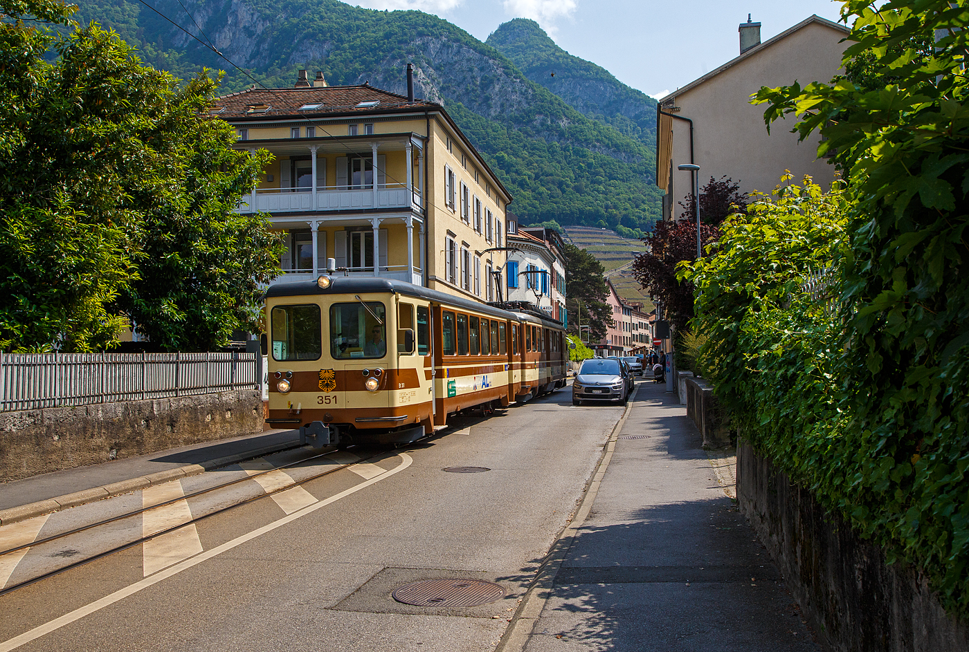 Die Straßenbahn von Aigle kommt:
Der AL Regionalzug von Leysin nach Aigle fährt am 28. Mai 2023 (hier als Straßenbahn) durch Altstadt und erreicht bald den Bahnhof Aigle. Der Zug besteht aus dem führenden Steuerwagen AL Bt 351 „Aigle“  und dem Triebwagen AL BDeh 4/4 302 „Leysin“, beide sind noch im ursprünglichen Anstrich der AL (es sind auch die einzigen). 

In Aigle (Waadt) gibt es gleich drei Schmalspurbahnen, die seit 1999 in die Transports Publics du Chablais (TPC) fusioniert worden sind, so machten wir auf unserer Rückreise hier mal einen kurzen Zwischenhalt. Die Schmalspurbahnen sind die Aigle–Ollon–Monthey–Champéry-Bahn (AOMC), die Aigle–Sépey–Diablerets-Bahn (ASD), seit dem 22. Dezember 1913 und die Aigle–Leysin-Bahn (AL).

Die Chemin de fer Aigle–Leysin (AL), deutsch Aigle-Leysin-Bahn, war eine Eisenbahngesellschaft im Schweizer Kanton Waadt. Ihre von 1900 bis 1916 eröffnete 6,2 Kilometer lange Strecke führt von Aigle im Rhonetal hinauf nach Leysin-Grand Hôtel. Die gemischte Zahnradbahn in der Spurweite 1.000 mm (Meterspur) mit dem System Abt wird seit der Betriebsaufnahme elektrisch betrieben. Im Jahr 1999 fusionierte die AL zu den Transports Publics du Chablais (TPC).

Die Bahnstrecke Aigle–Leysin hat ihren Ausgangspunkt vor dem SBB-Bahnhof und führt als Straßenbahn auf der Rue de la Gare (Bahnhofstraße), der Avenue des Ormonts und über die Grande Eau zum Kopfbahnhof Aigle-Dépôt. Dort ändern die Züge die Fahrtrichtung, damit das Triebfahrzeug für die anschließende Bergfahrt am Ende des Zuges eingereiht ist. 

Im Keilbahnhof Aigle-Dépôt beginnt der 5,3 Kilometer lange und bis zu 230 Promille steile Zahnstangenabschnitt. Zunächst führt er durch die Rebberge und bietet den Fahrgästen einen Ausblick auf das Rhonetal. Bei der Haltestelle Pont-de-Drapel wechselt die Vegetation und das Trassee befindet sich nun im Wald. Der Zug erreicht eine Waldlichtung mit dem Bahnhof Rennaz (Leysin), wo er sich in der Regel mit dem Gegenzug kreuzt. Die Strecke führt weiter durch Wald und den 154 Meter langen Tunnel Rennaz. Ab rund 1.200 Meter über Meer fährt die Zahnradbahn durch Weiden und erreicht nach kurzer Zeit den Bahnhof Leysin-Village (Leysin-Dorf). Hier beginnt der Doppelspurabschnitt mit der 128 Meter langen Brücke Leysin nach Leysin-Feydey. Nach dem 287 Meter langen Kehrtunnel Leysin erreicht die Strecke, immer noch mit Zahnstange versehen, den Endpunkt Leysin-Grand Hôtel.